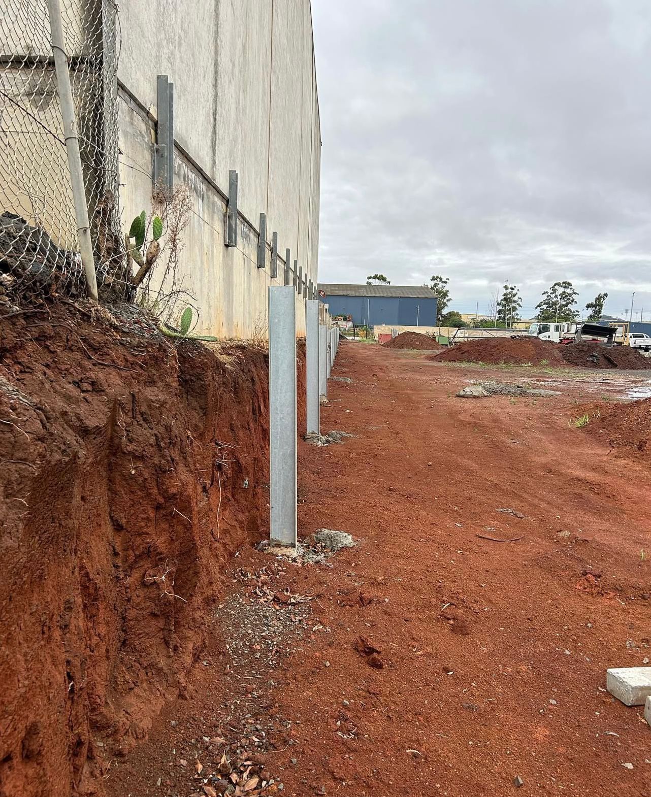 Construction Site With Metal Poles Along a Building Wall and Red Soil — Chief Structural Landscaping In Glenvale, QLD