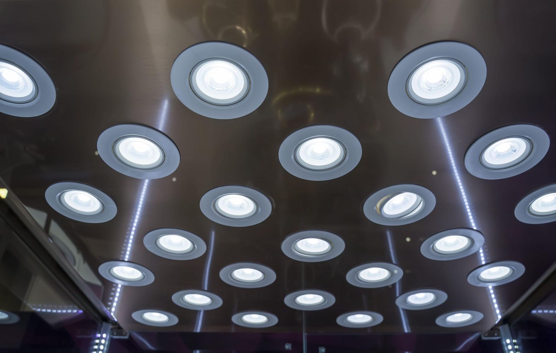 Ceiling with many recessed circular lights, some with LED strips; reflective surface.