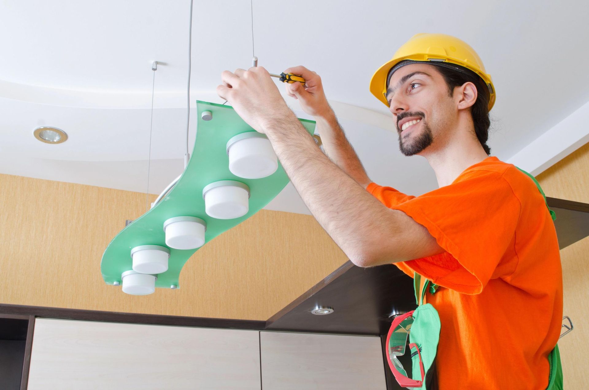 Electrician installing a modern light fixture in a kitchen, smiling.