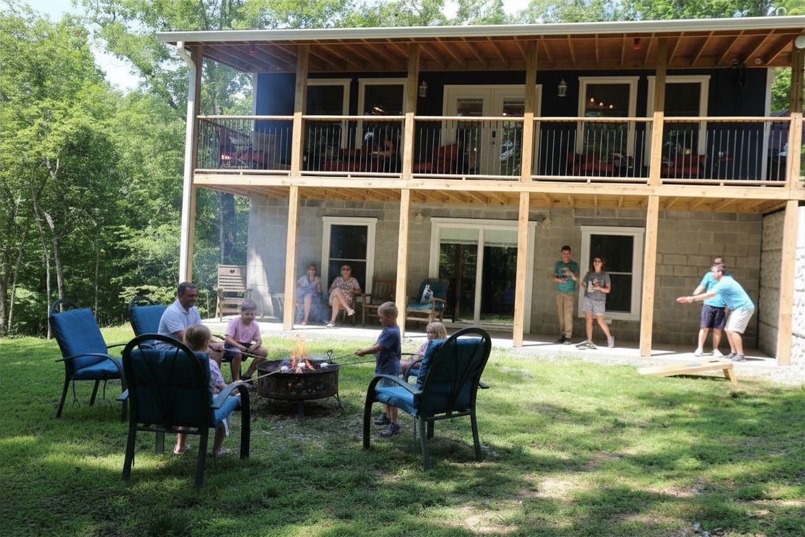 Blue Haven Paradise People relaxing in lawn chairs outside a two-story house with a wooden porch and trees in the yard.