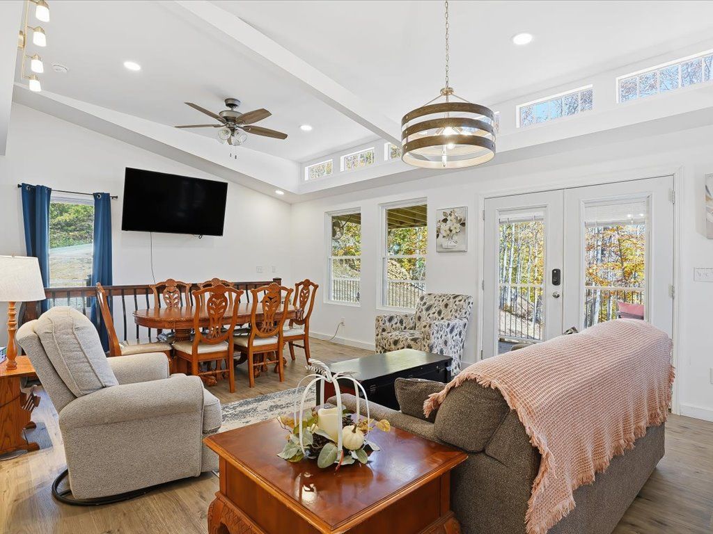Bright open living room with gray sofa, armchair, dining table, wall TV, and French doors to a patio