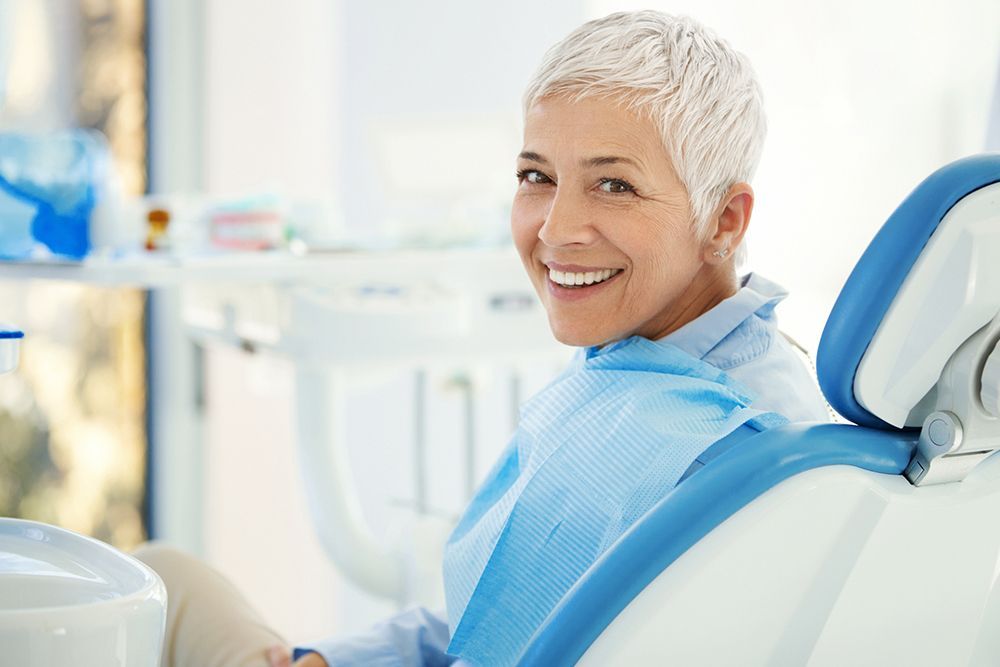 A woman is smiling while sitting in a dental chair.
