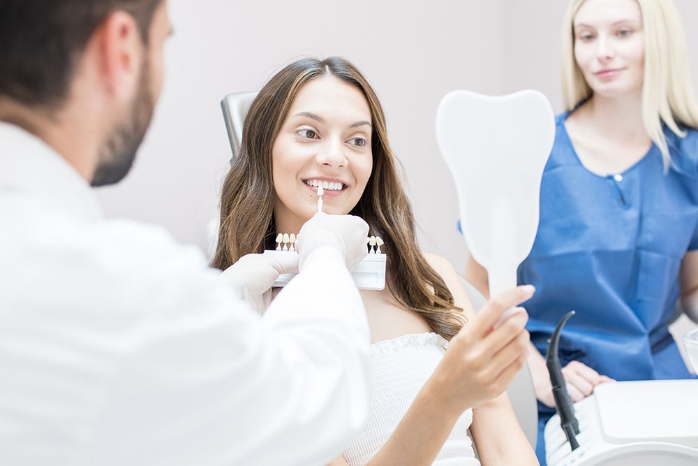 A woman is sitting in a dental chair looking at her teeth in a mirror.