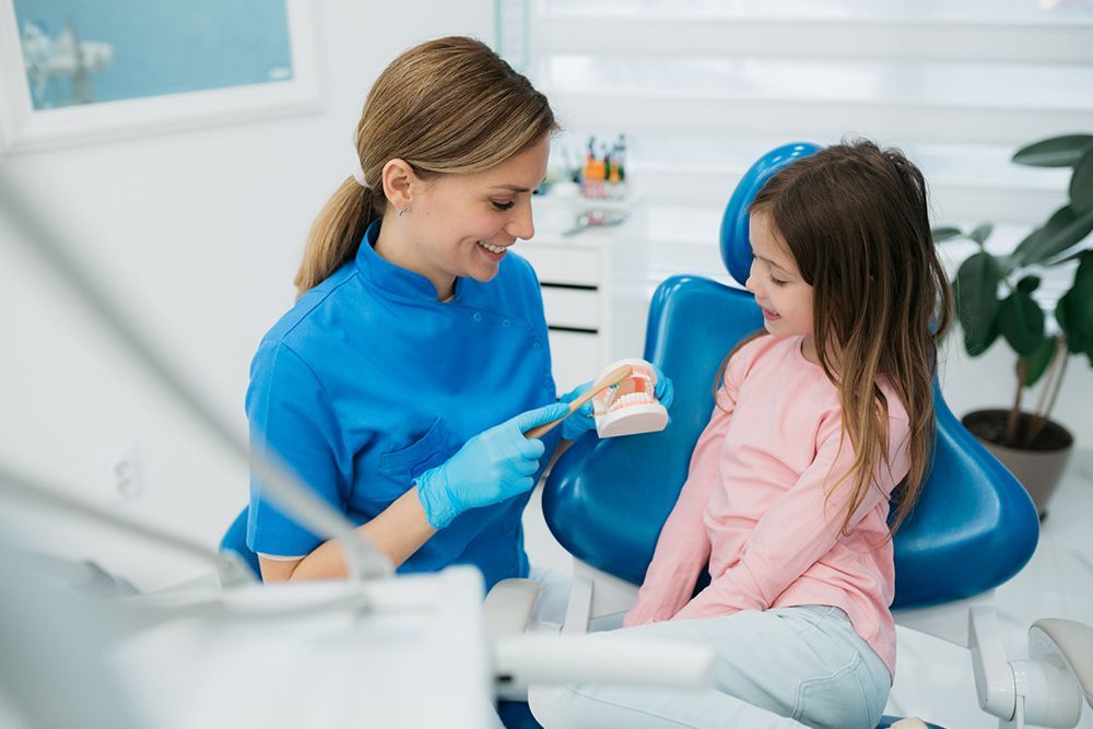 A little girl is sitting in a dental chair while a dentist examines her teeth.