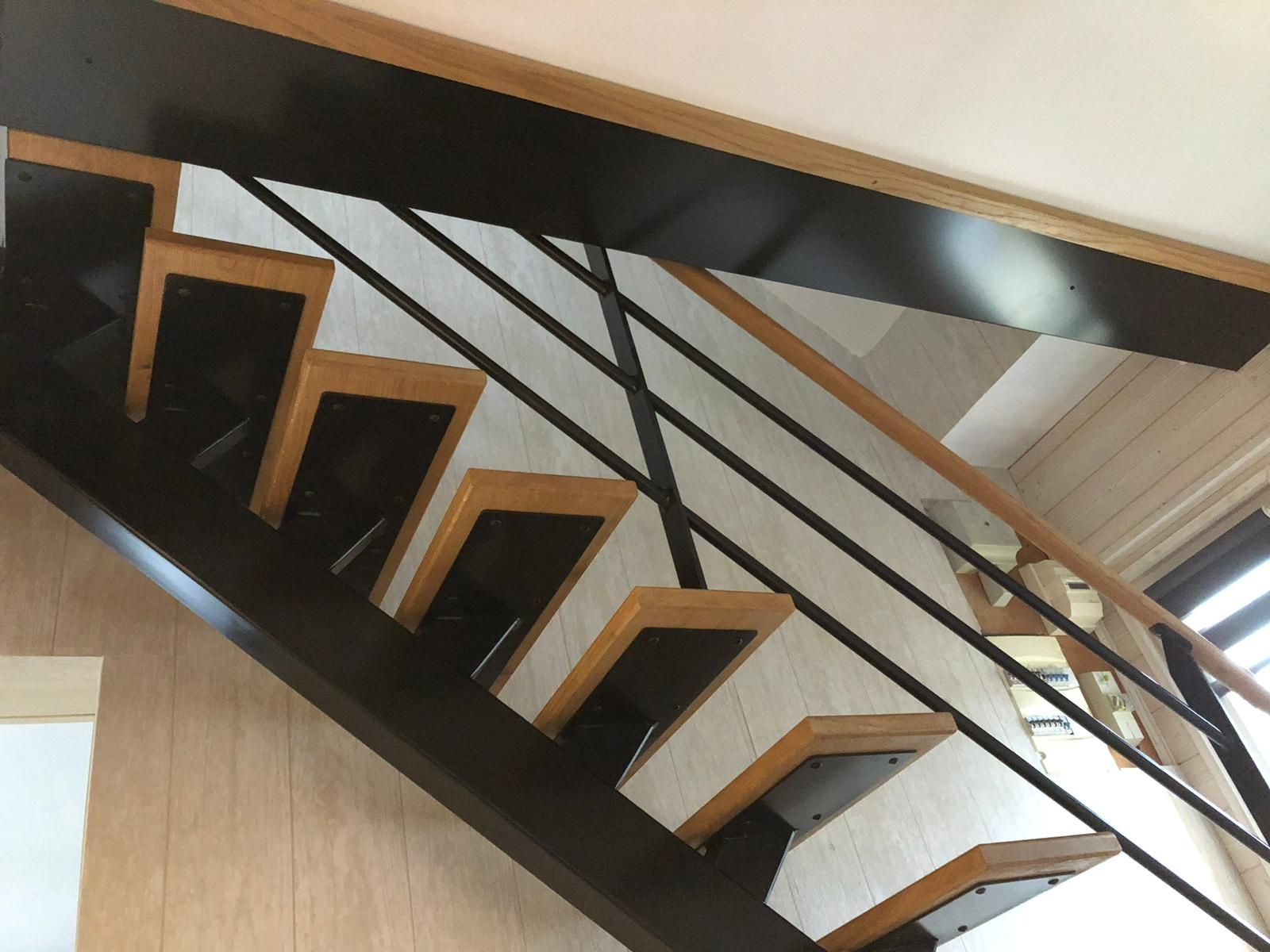 Escalier avec marches en bois et structure en métal noir, rampe en bois, menant vers le haut, près d'un mur.