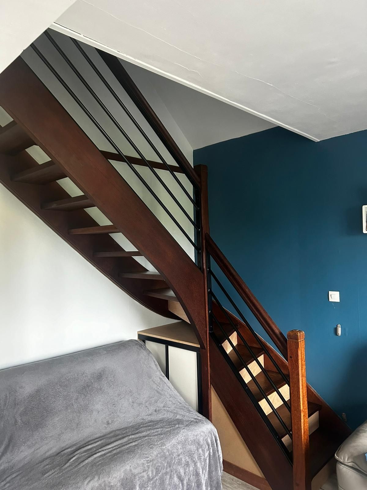 Escalier en bois avec des barreaux en métal noir, montant sur des murs blancs et bleu sarcelle.
