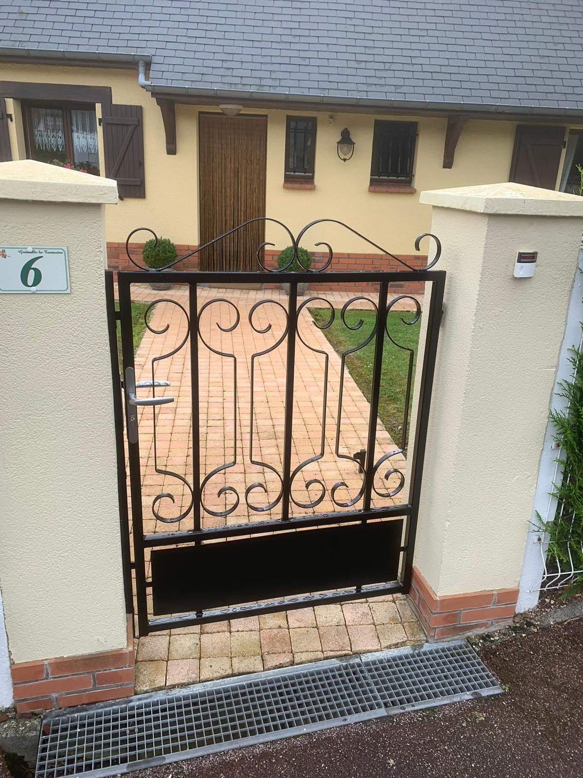 Portail en fer forgé noir à l'entrée d'une maison avec des accents de stuc beige et de brique.