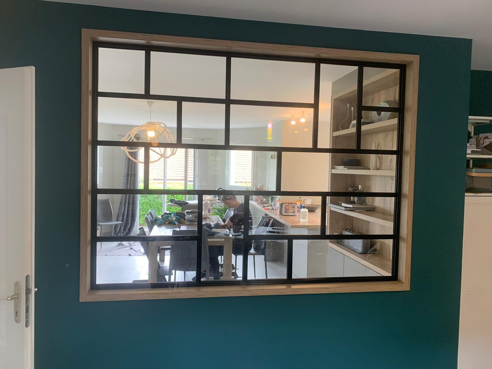 Miroir à motif de grille noire, encadré de bois, sur un mur bleu sarcelle, reflétant une salle à manger.