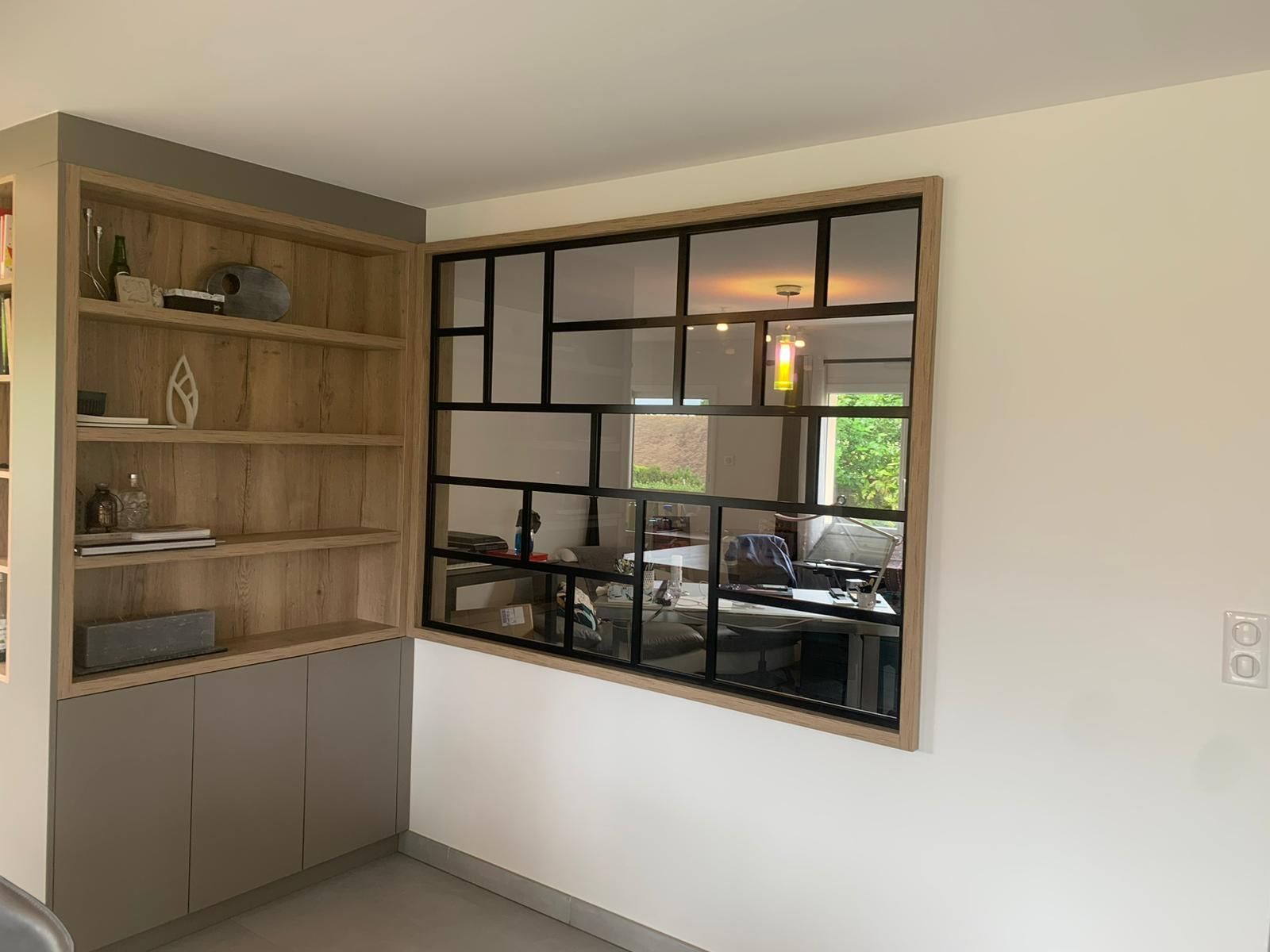 Étagères et armoires intégrées à côté d'une fenêtre avec un design en grille noire et un cadre en bois.