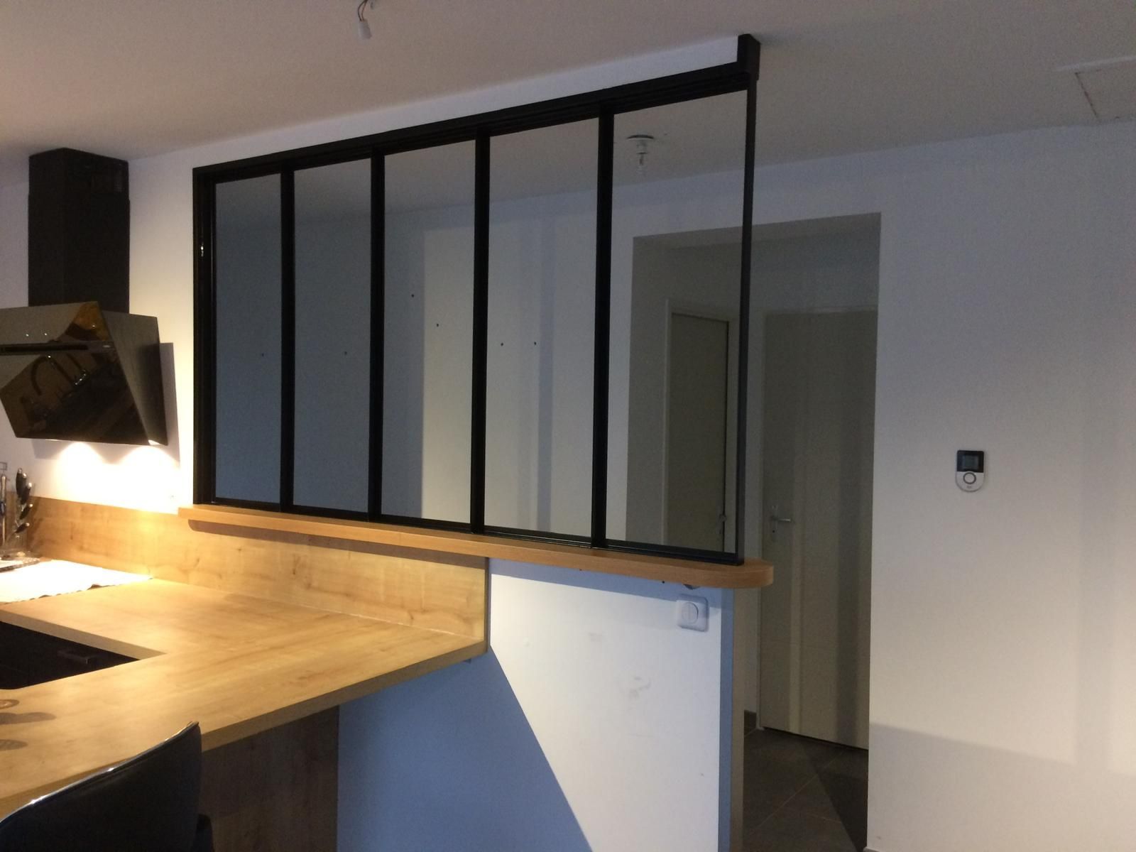 Cloison vitrée à cadre noir entre cuisine et couloir, plan de travail en bois.