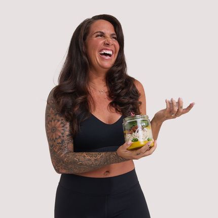 A woman is holding a jar of food and laughing.