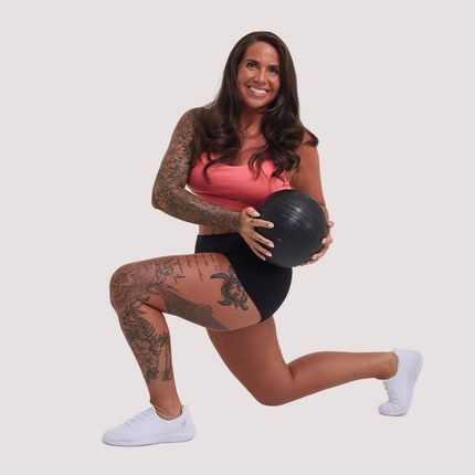 A woman with tattoos on her legs is holding a black ball - Average Jenn's - Personalized Workout and Nutrition Plans