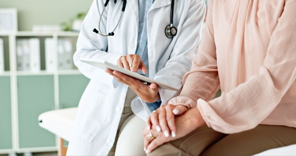 A doctor is holding the hand of a patient while looking at a tablet.