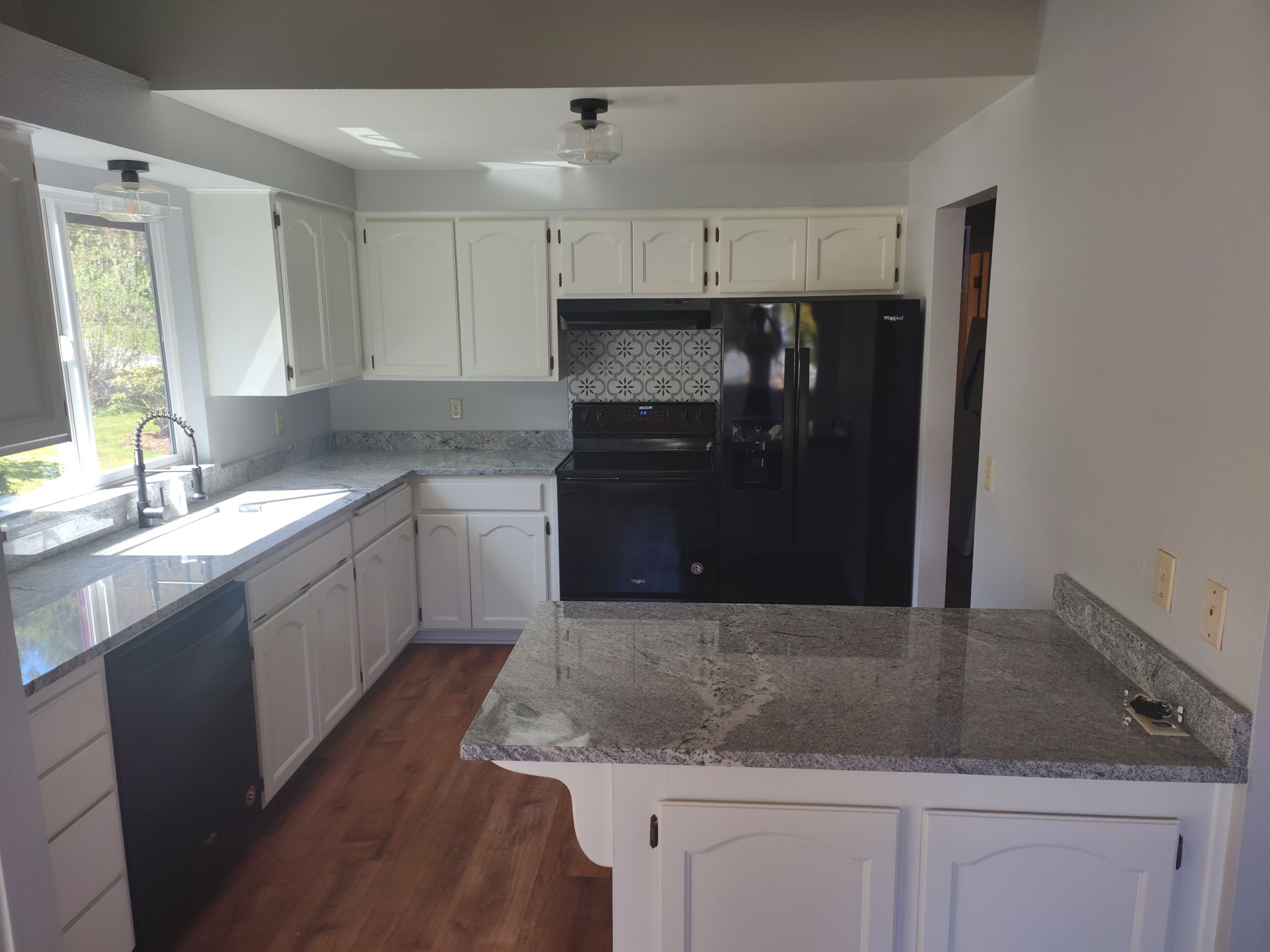 A kitchen with white cabinets , granite counter tops , and a black refrigerator.