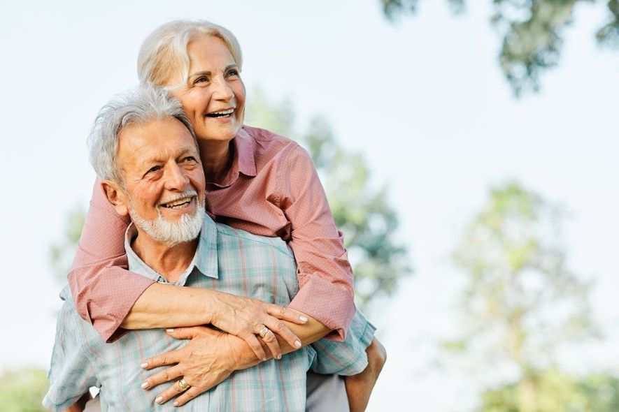 A man is giving a woman a piggyback ride in a park.
