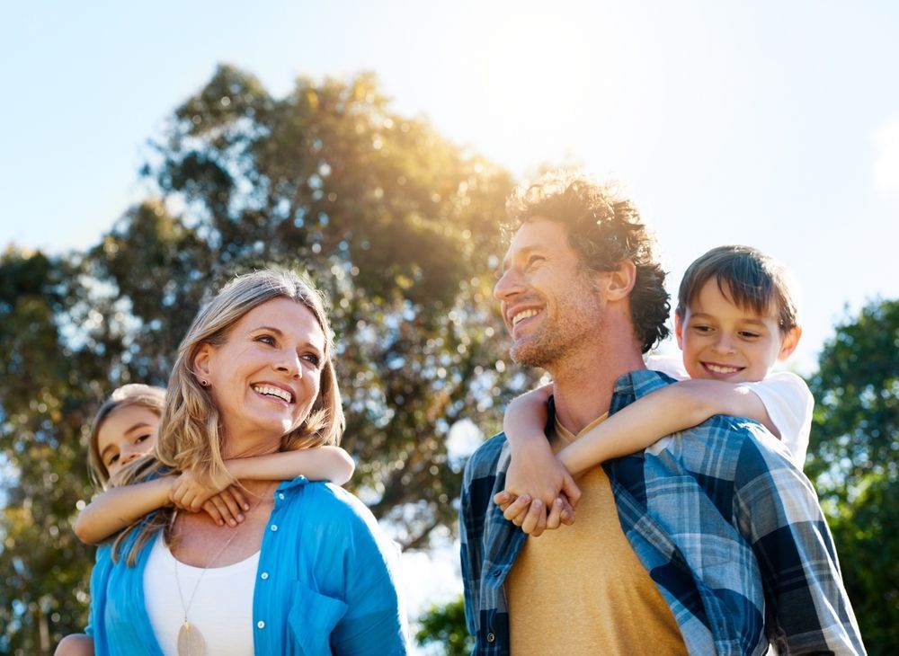 A family is walking in a park with a man carrying two children on his shoulders.