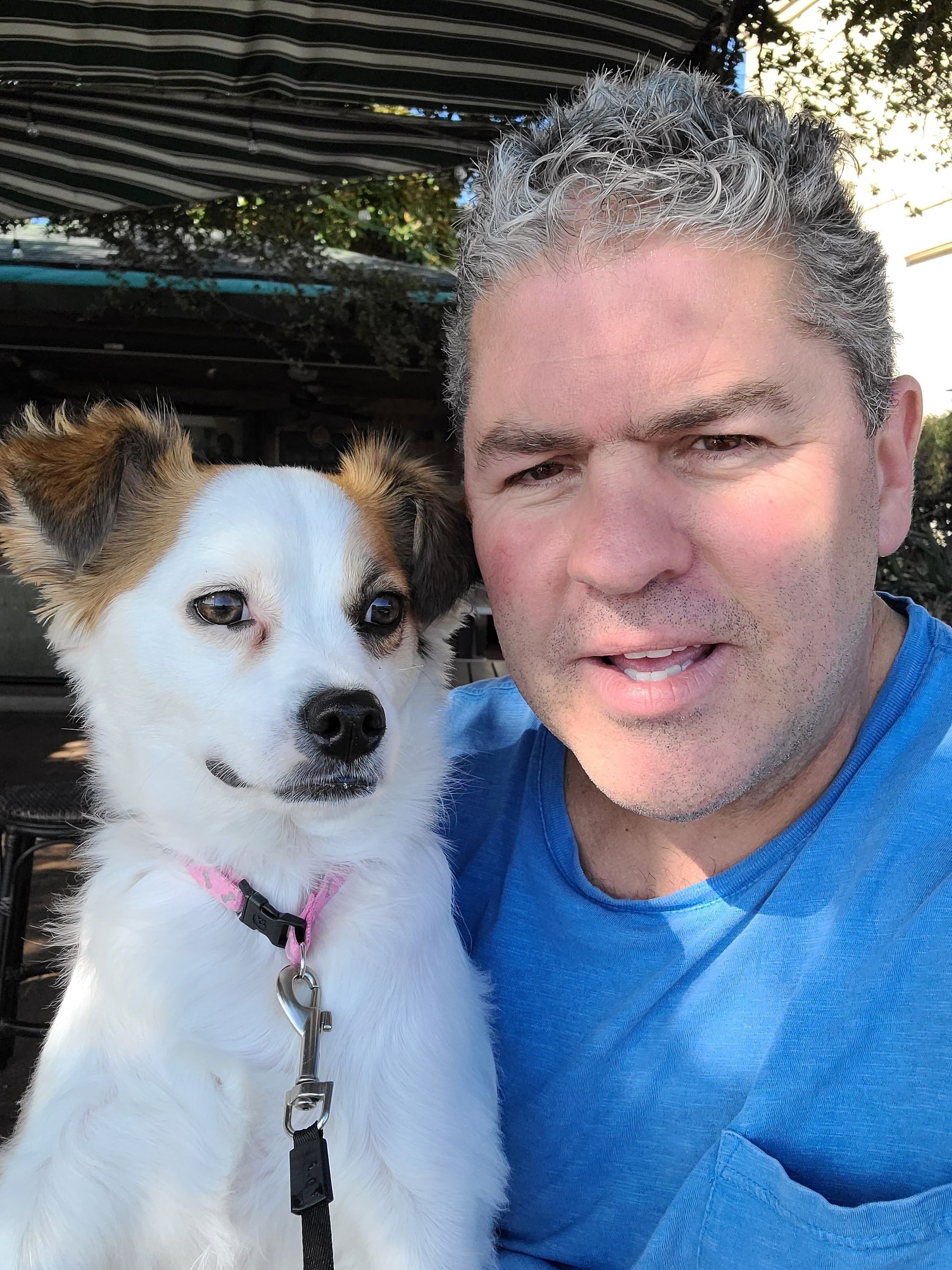 A man in a blue shirt is holding a white dog.