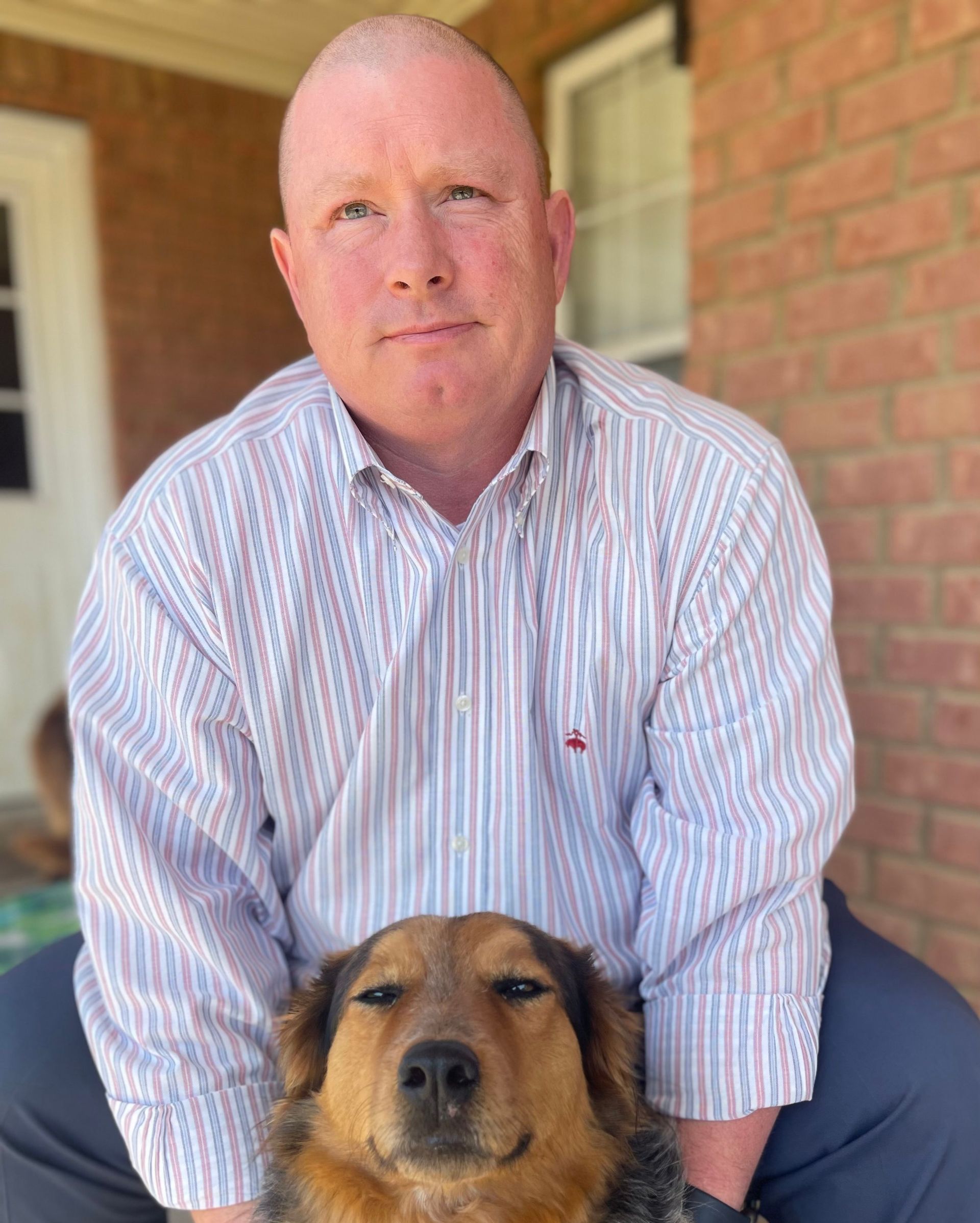 A man is sitting on a porch with a dog on his lap.