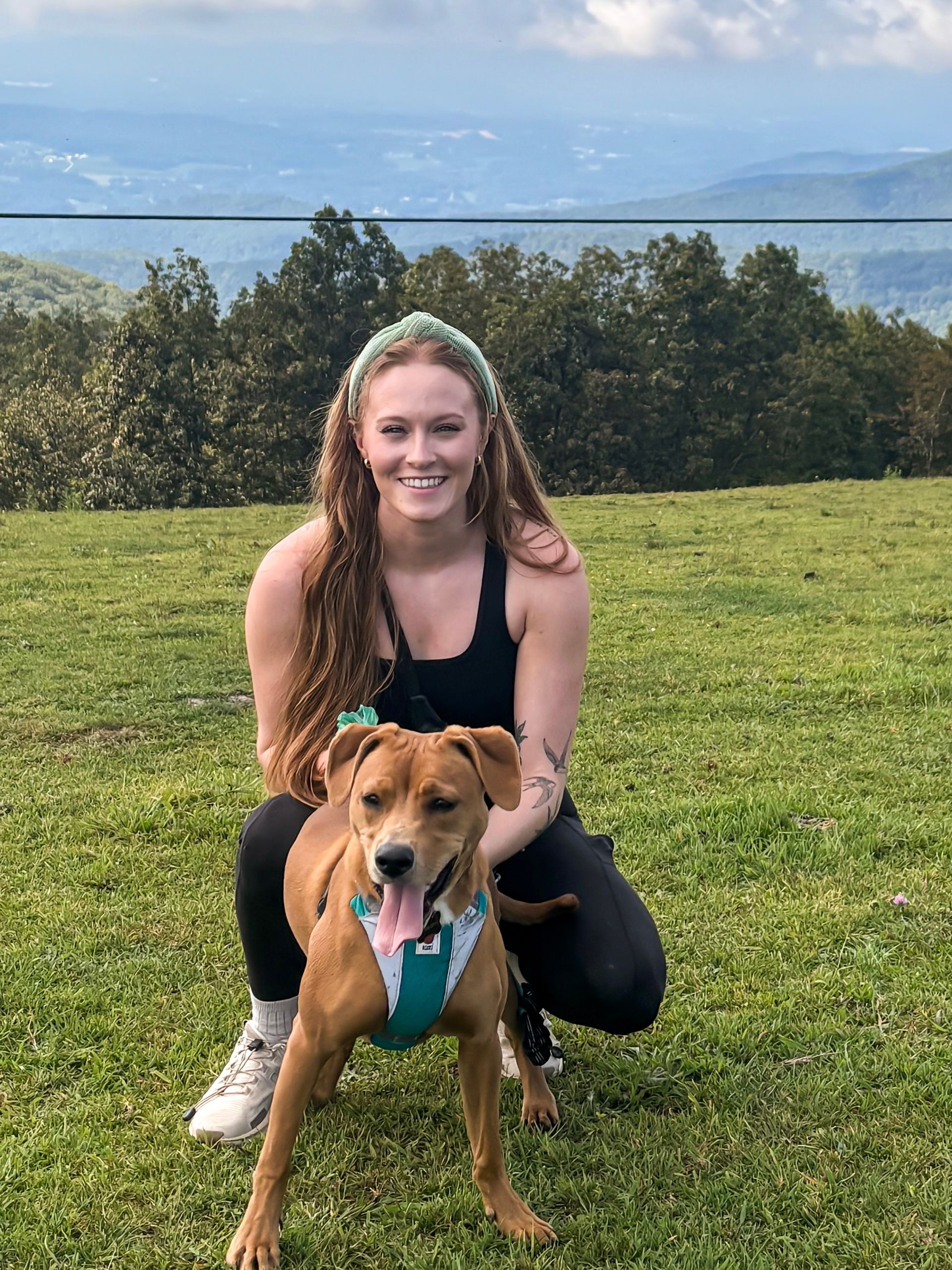A woman is kneeling down next to a brown dog in a field.