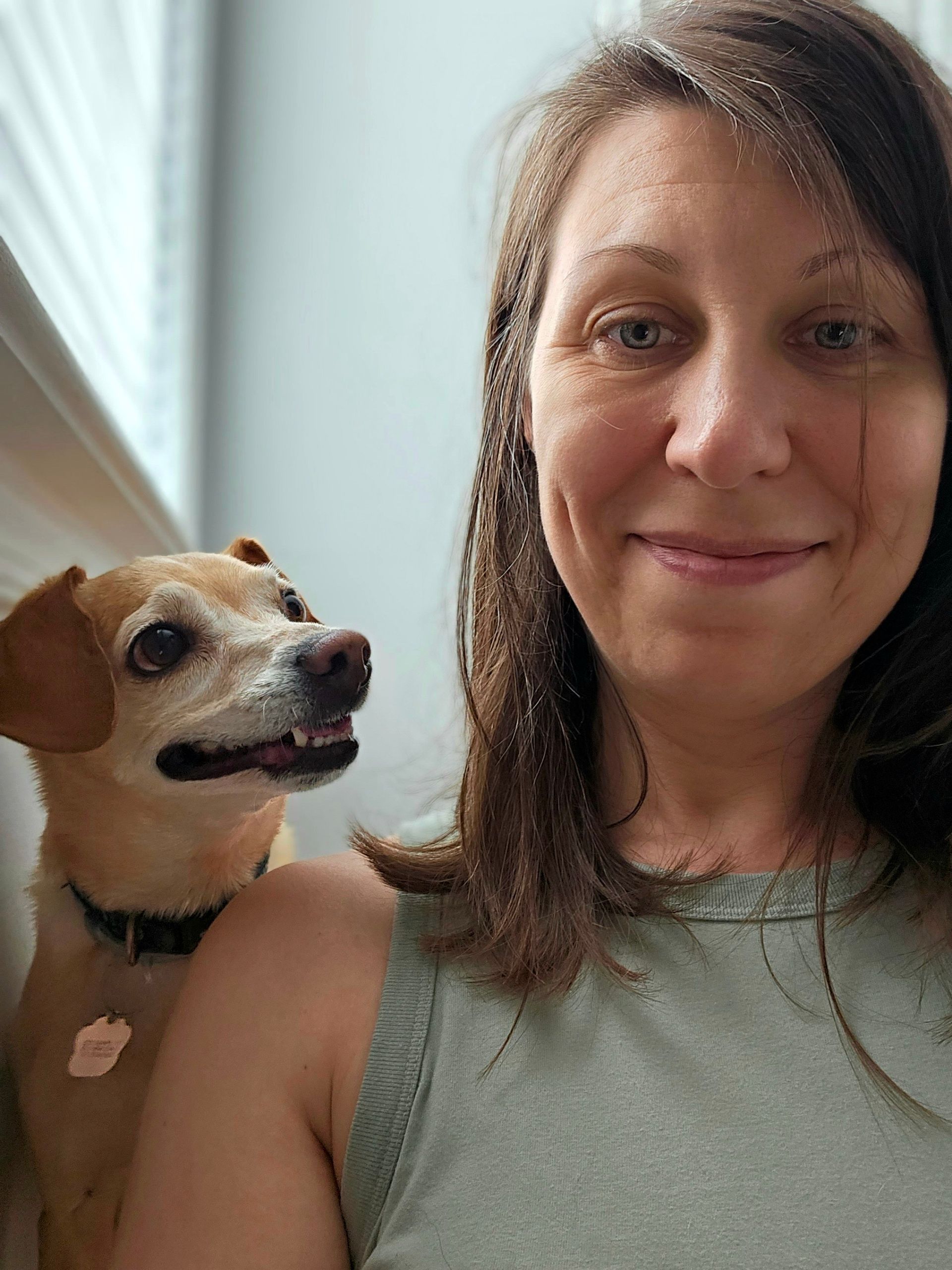 A woman is holding a small dog on her shoulder.