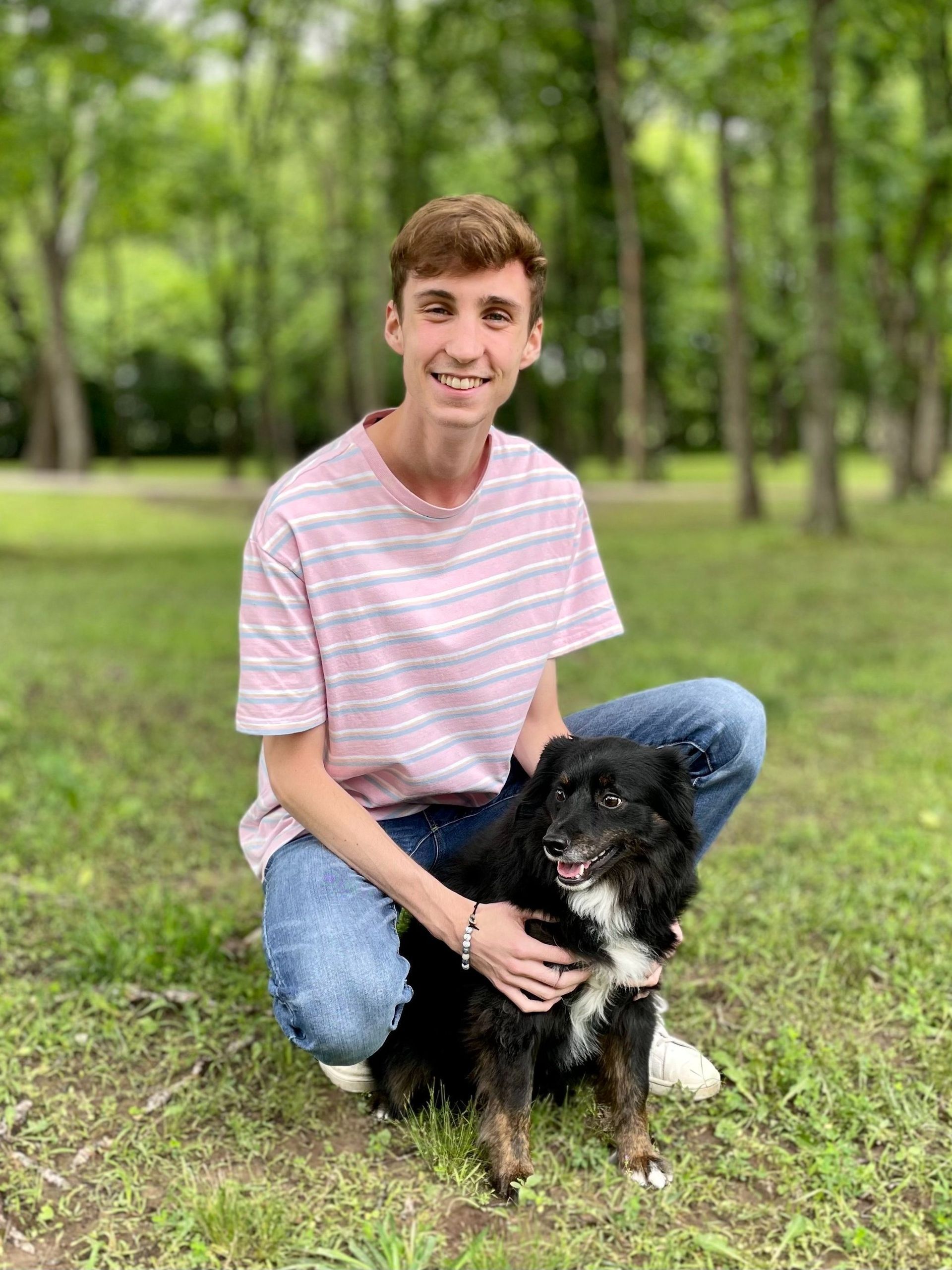 A young man is kneeling down next to a dog in a park.