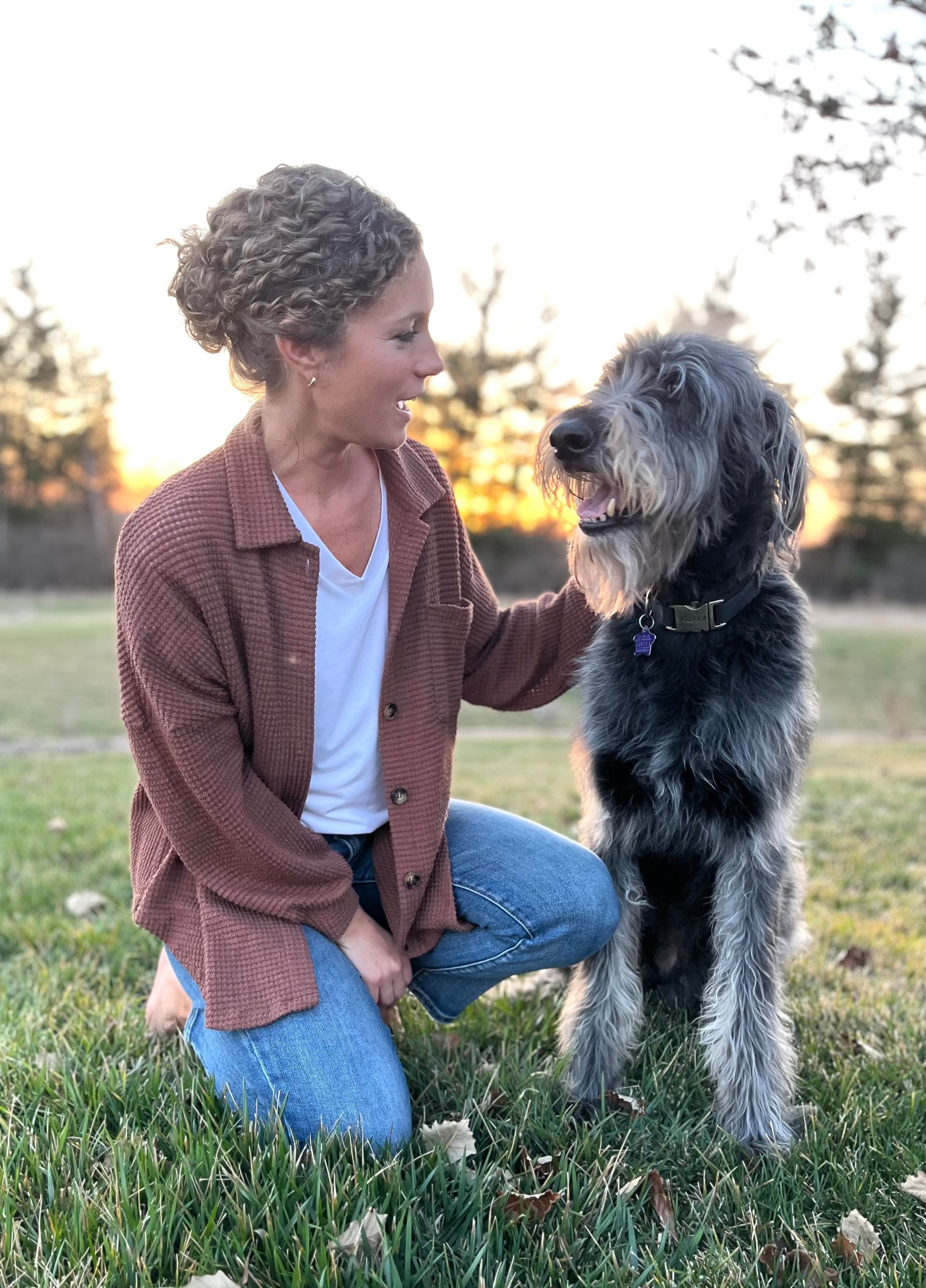 A woman is kneeling down next to a dog in the grass.