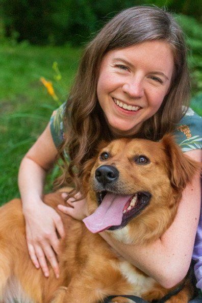 A woman is holding a brown dog in her arms and smiling.