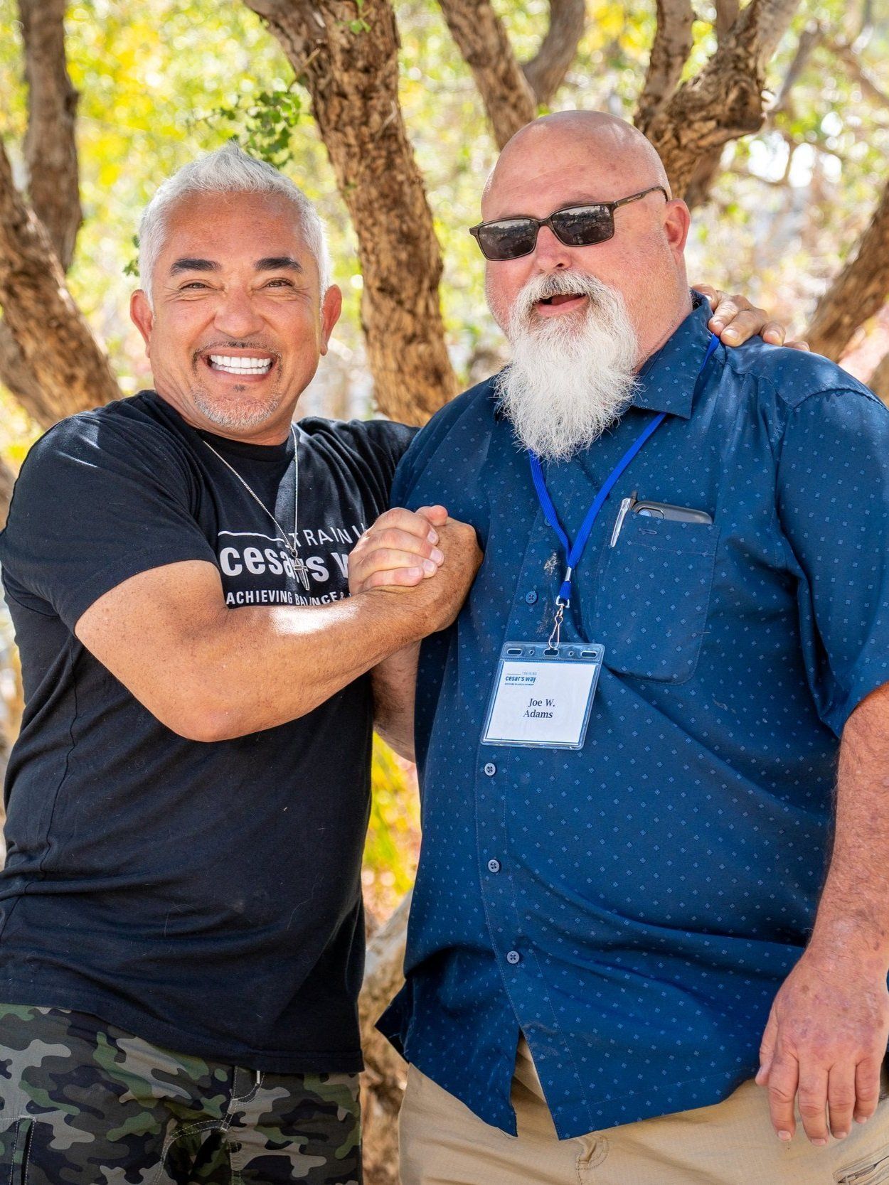 Two men are shaking hands in front of a tree.