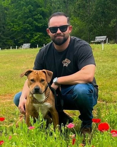 A man is kneeling down next to a dog in a field of flowers.