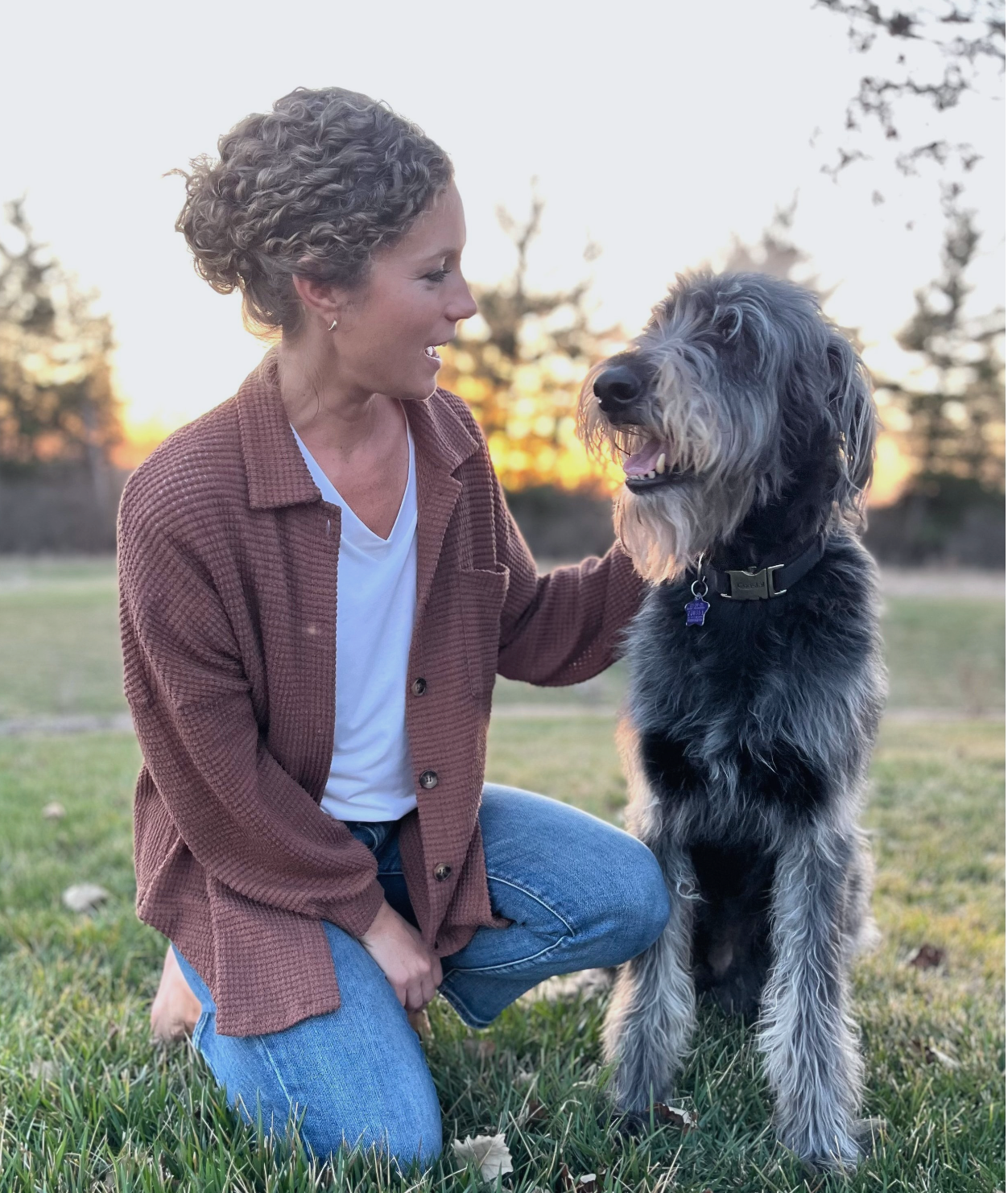 A woman is kneeling down next to a dog in a field.