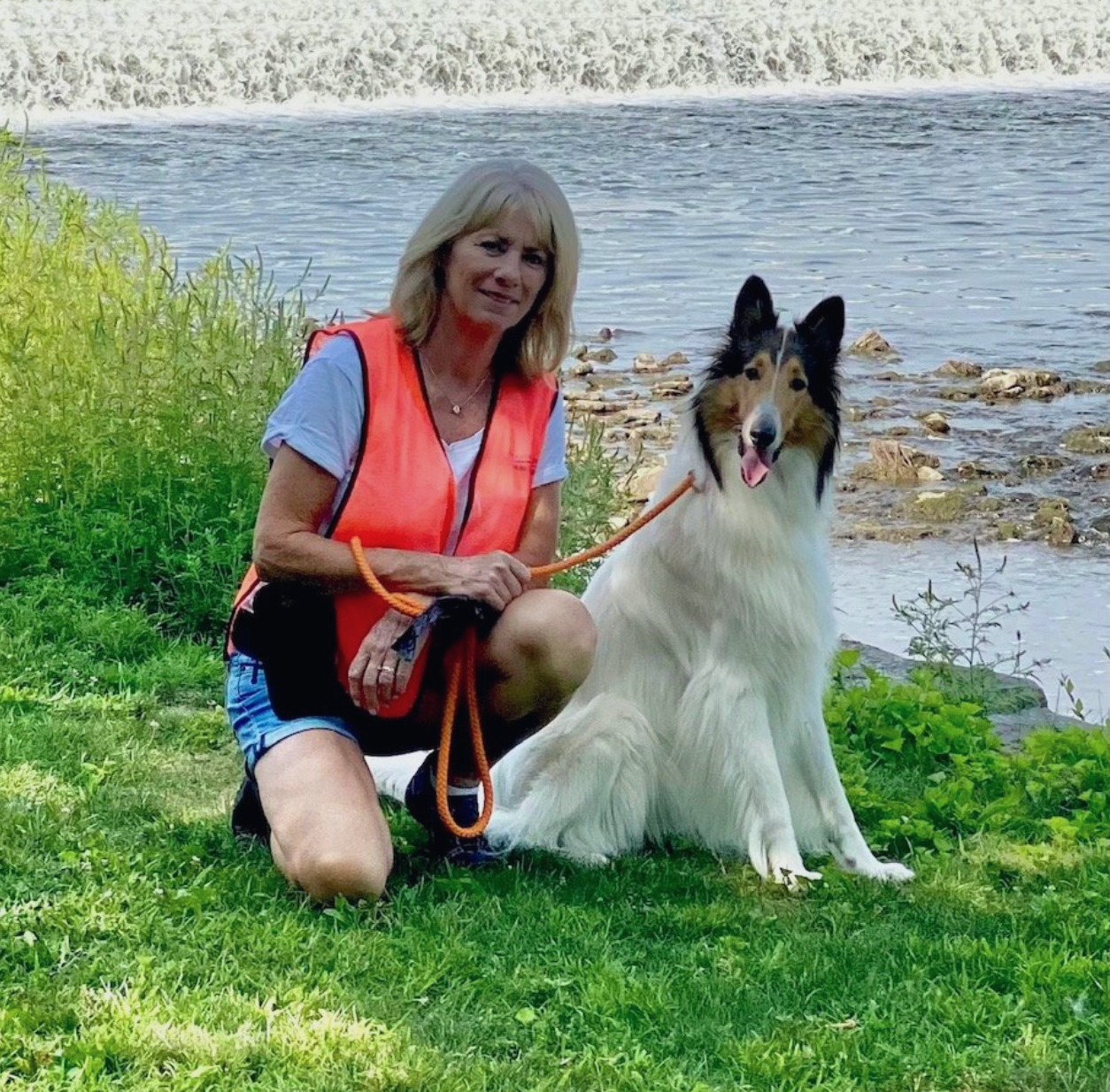 A woman is kneeling down next to a collie dog on a leash