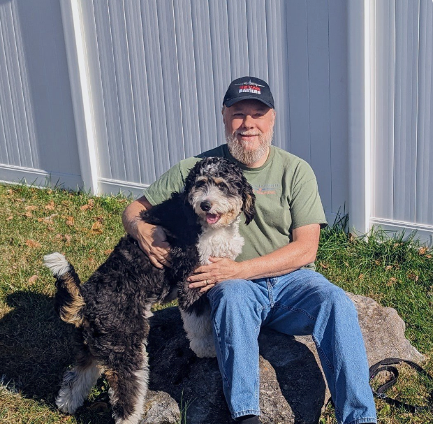 A man is sitting on a rock holding a small black and white dog