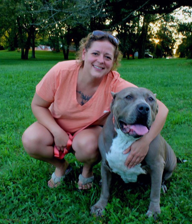 A woman is kneeling down next to a dog in the grass