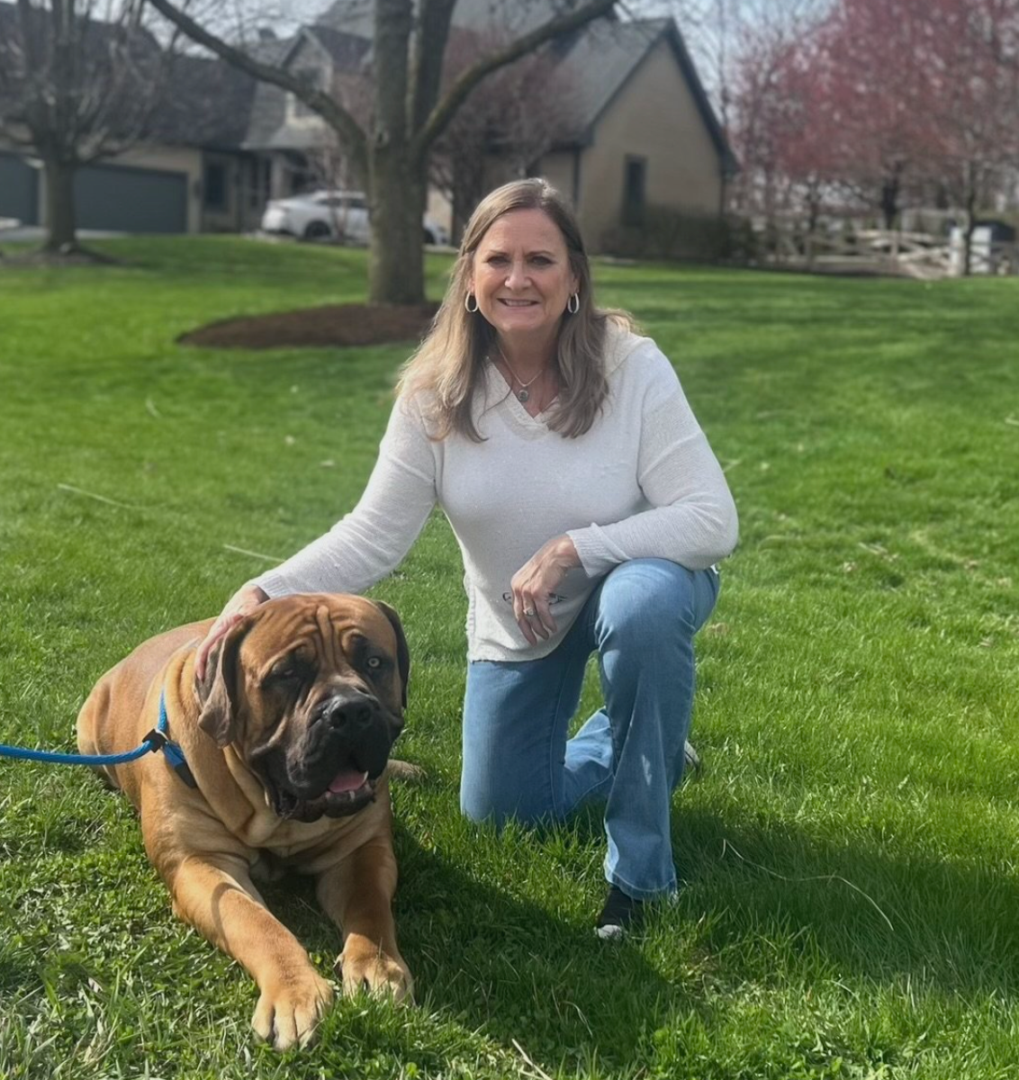 A woman is kneeling down next to a brown dog on a leash