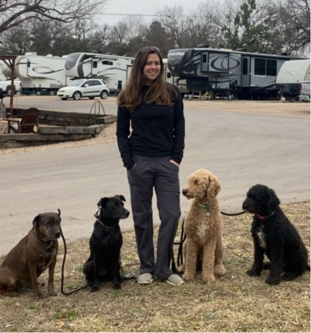 A woman standing next to three dogs with a trailer in the background