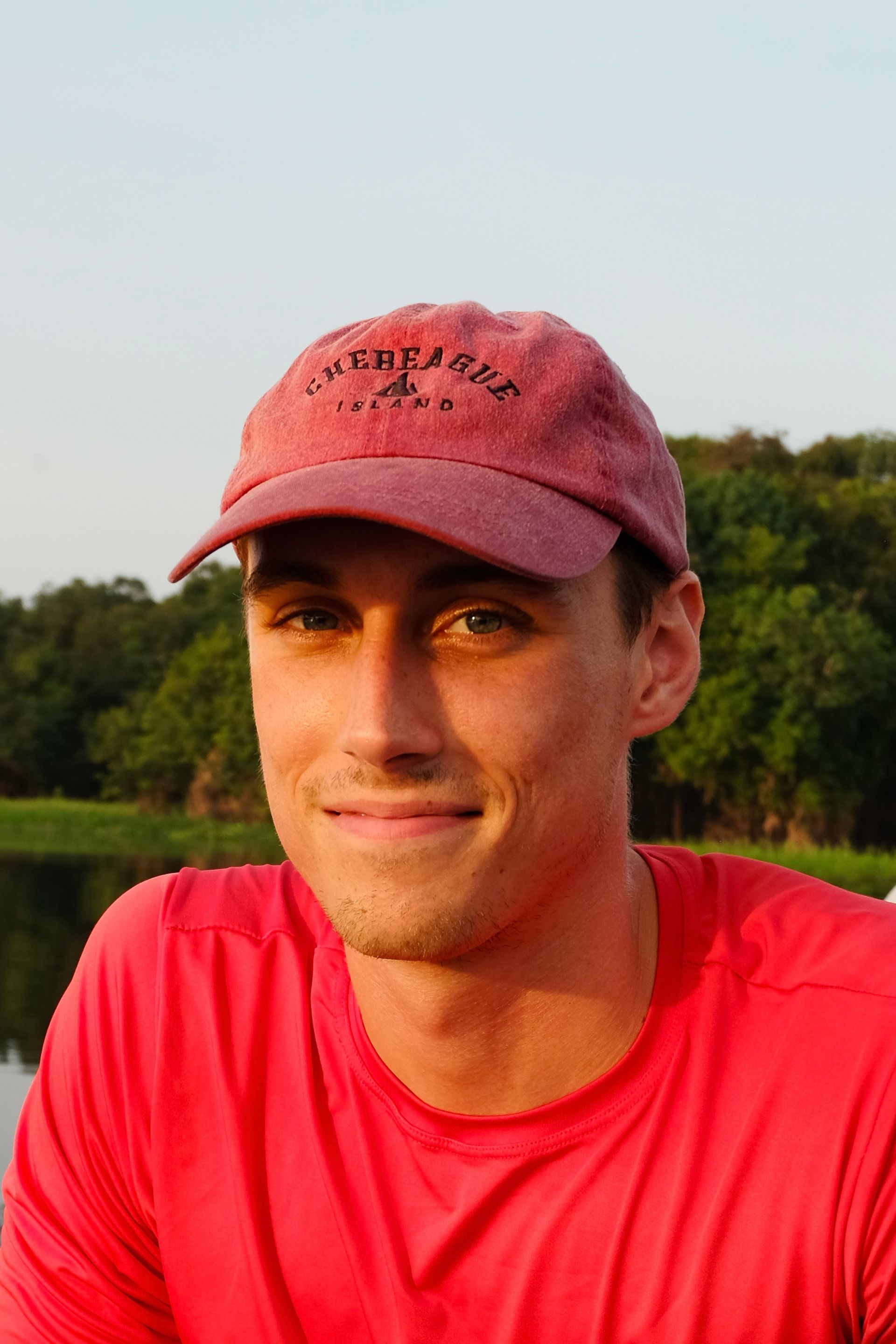 Man in a red cap and shirt smiles outdoors.