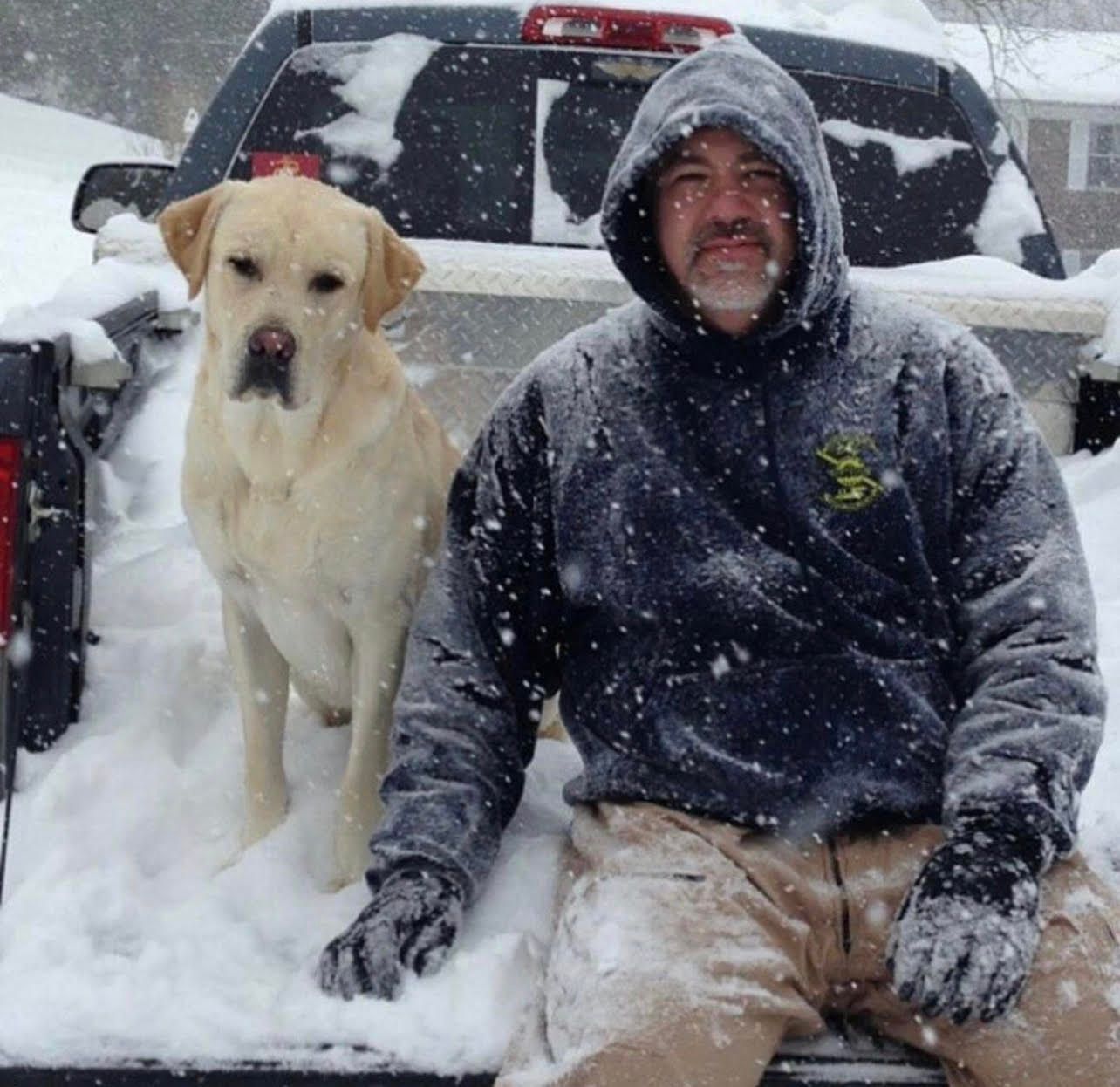 A man is sitting on a rock holding a small black and white dog