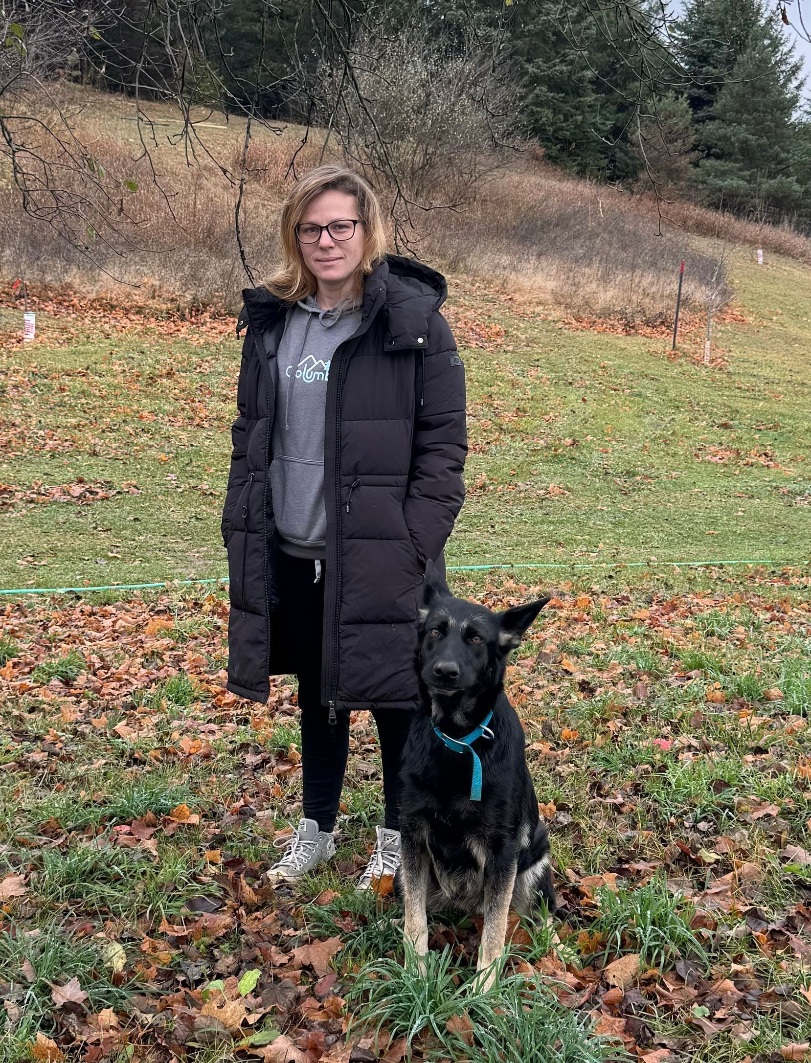 A woman is standing next to a black dog in a field.