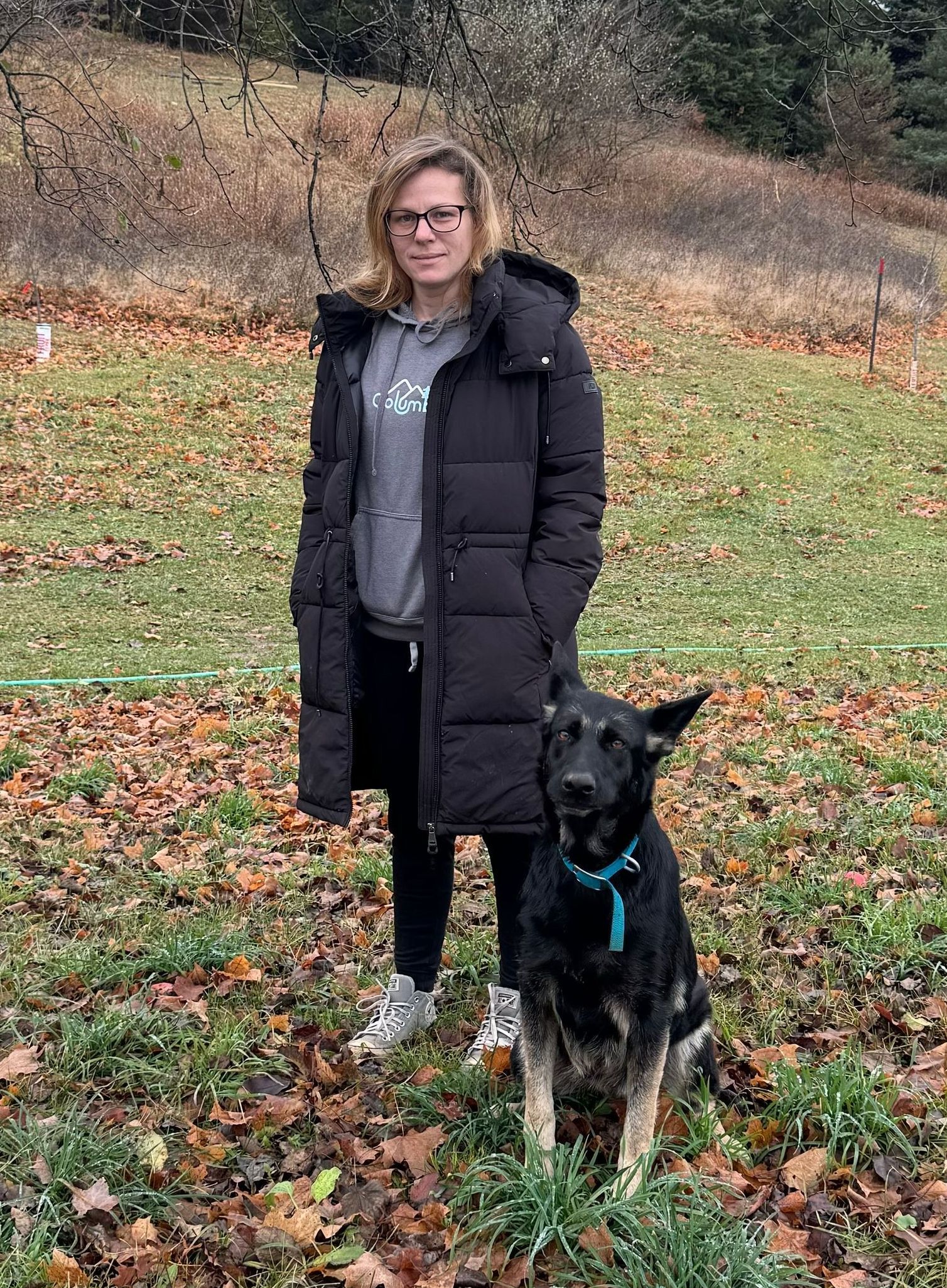 A woman is standing next to a black dog in a field.