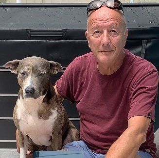 A man is sitting next to a dog wearing sunglasses.