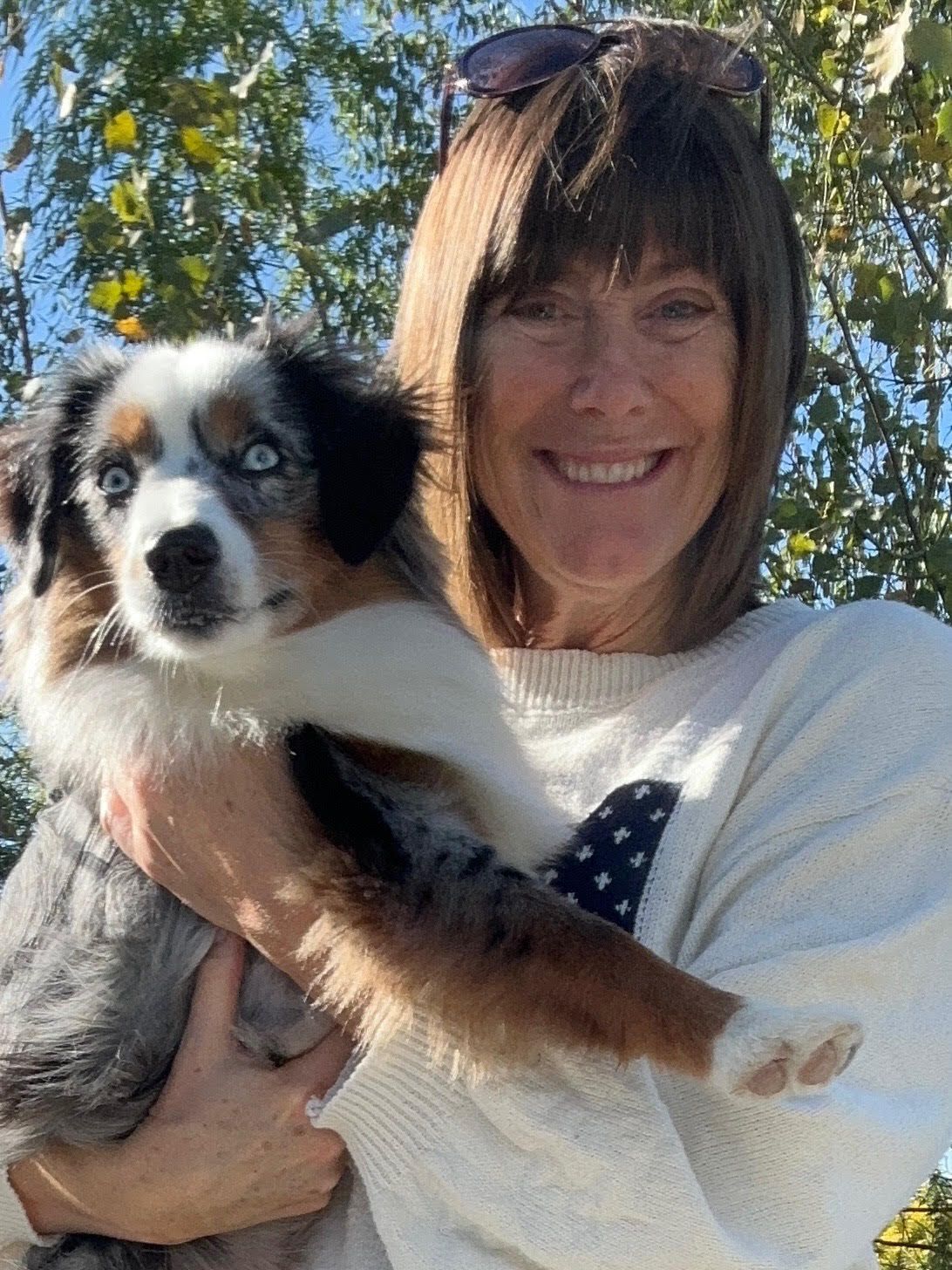 Woman smiling, holding a blue merle Australian Shepherd puppy outdoors.