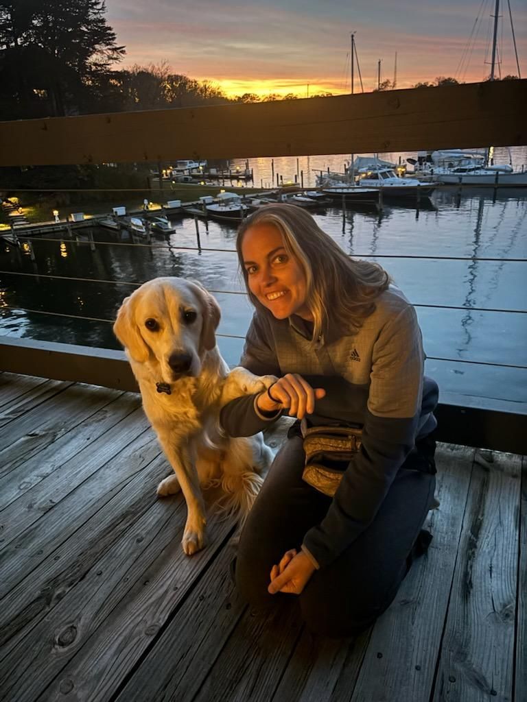 A woman is kneeling down next to a dog on a deck.