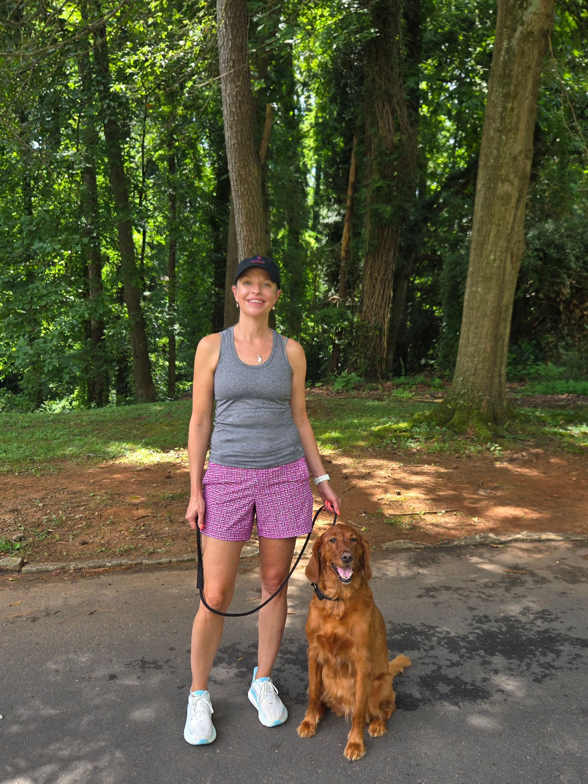 A woman is sitting on a dock with a dog wearing a life jacket.