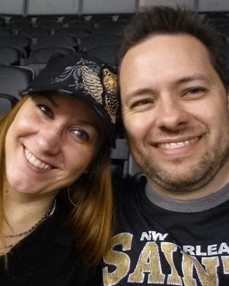 A man and a woman are posing for a picture and the man is wearing a saints shirt