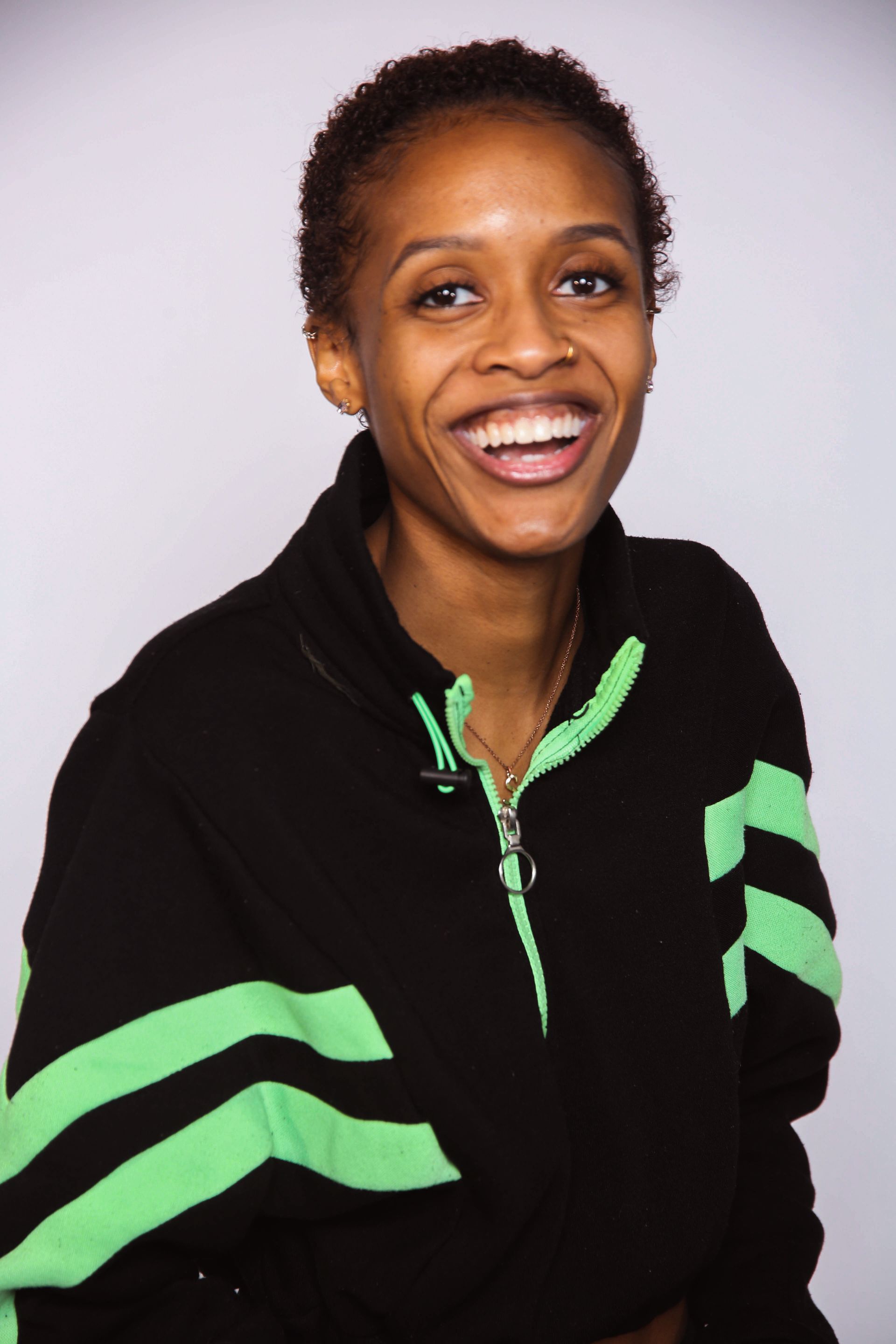 Smiling woman with short hair in a black and green sweatshirt against a white background.