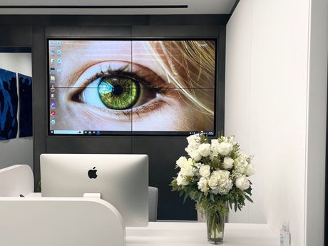 A computer monitor is sitting on a desk next to a vase of flowers.