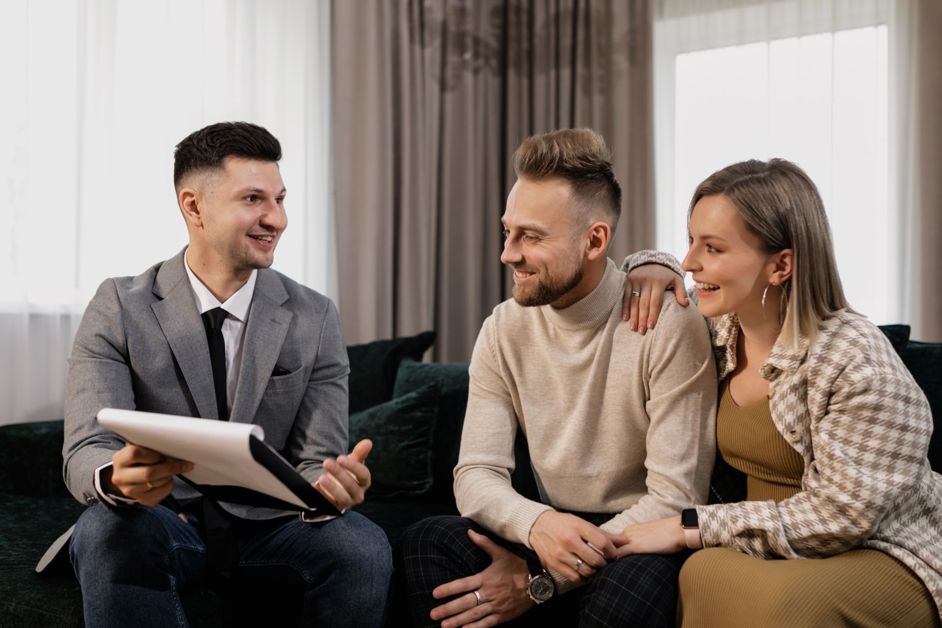 A real estate agent discusses documents with a couple sitting on a couch.