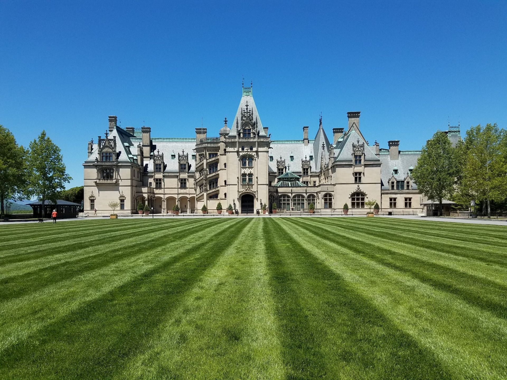 Biltmore Estate, large stone mansion with multiple towers and green lawn with striped mowing pattern under a blue sky.
