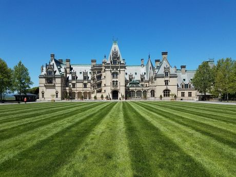 Biltmore Estate, large stone mansion with multiple towers and green lawn with striped mowing pattern under a blue sky.