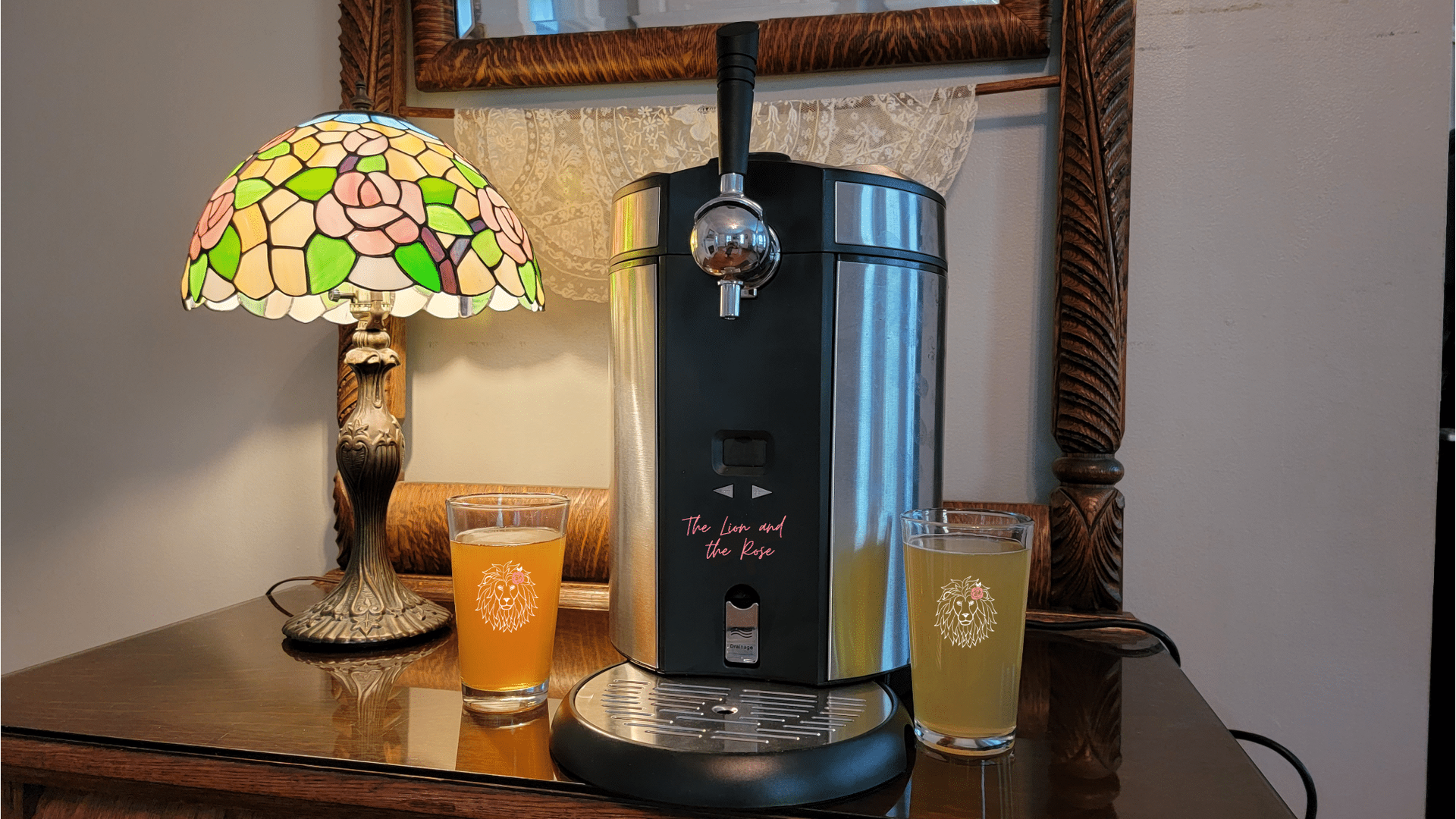 A beer tap system with two filled glasses, next to a stained-glass lamp, on a wooden surface.